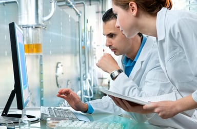 Technicians in lab coats looking at a monitor together