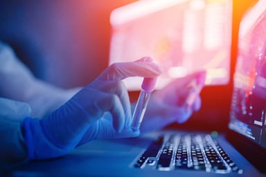 Gloved hands holding up vials over a laptop keyboard.