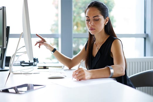 Woman pointing to a computer monitor and writing on a paper