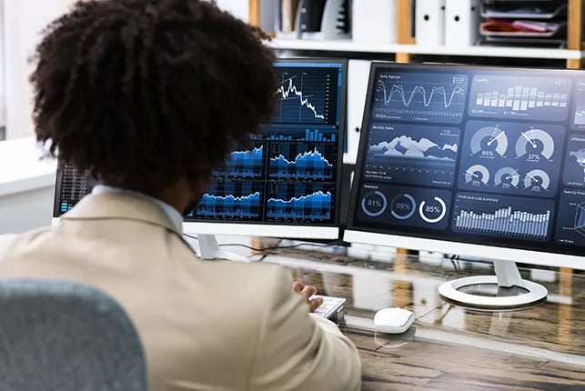 Person investigating data across two computer monitor screens.