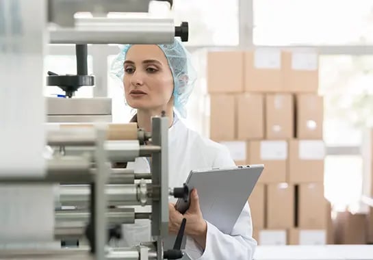 Woman using machinery and holding laptop