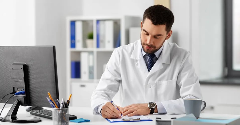 Doctor wearing lab coat and writing on clipboard at a desk in an office