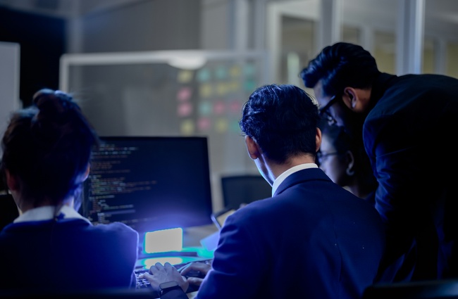 Development team reviewing source code on computer monitors in an office.