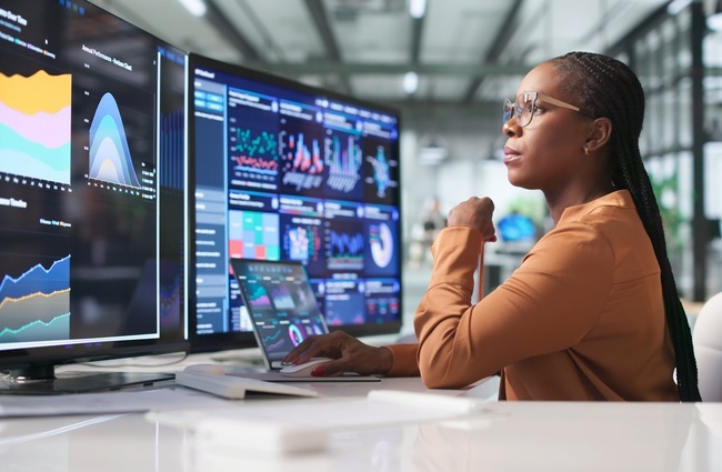 Professional reviewing business analytics dashboards across multiple monitors.