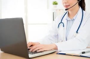 Healthcare professional writing on clipboard next to a laptop
