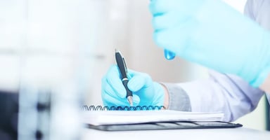 Hands wearing gloves writing in spiral notebook