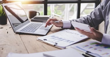 Man working with laptop, mobile phone, and worksheets