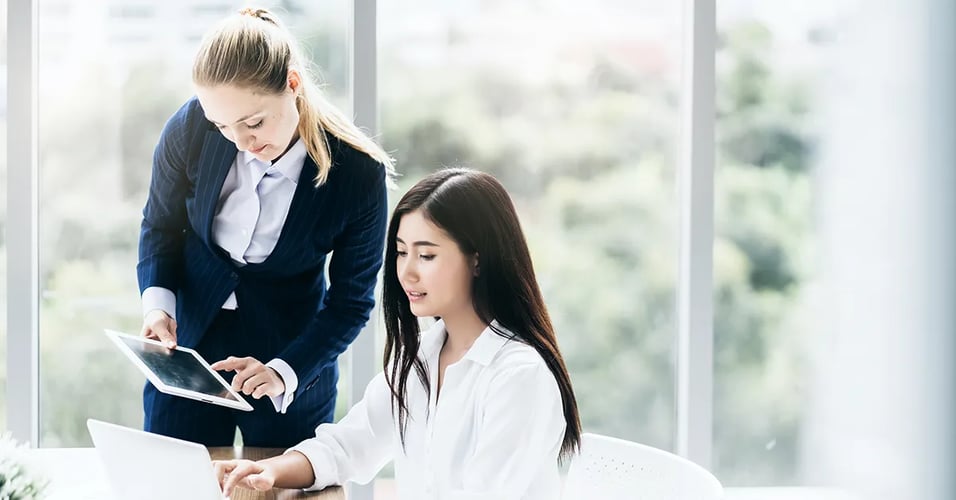 two-women-business-professionals-sharing-laptop-screen-and-tablet