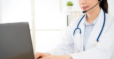 woman-in-lab-coat-wearing-headset-stethoscope-typing-on-laptop