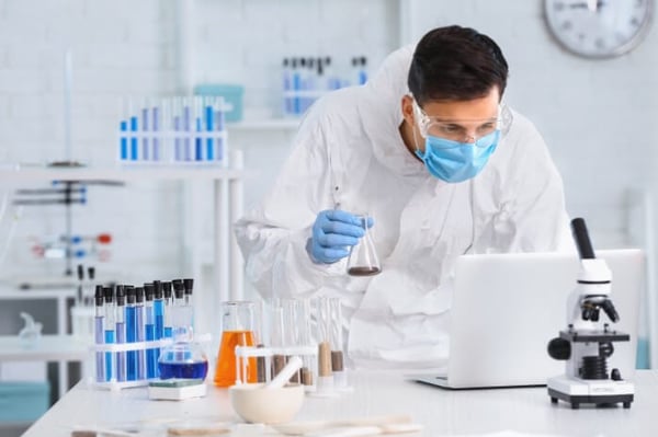 Lab technician holding a beaker and using a laptop