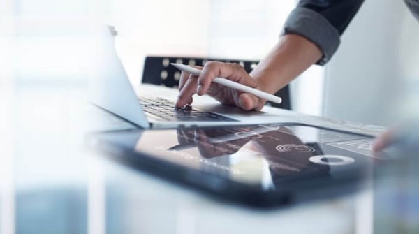 Person holding stylus while using a laptop and tablet