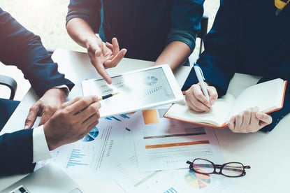 Hands pointing to graphs on a mobile table and writing in a paper notebook