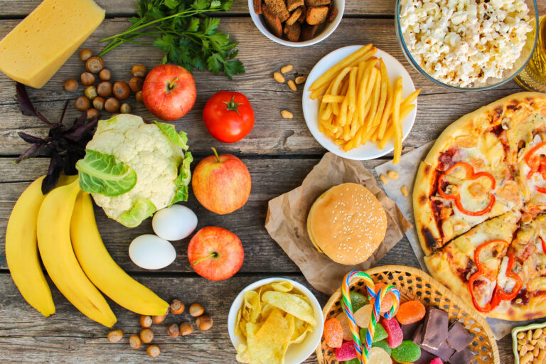 Many fruits, vegetables, hamburgers, french fries, and pizza on a picnic table.