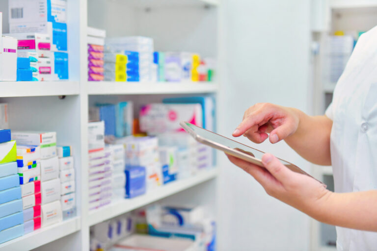 Person using mobile device in front of shelf of medicines.
