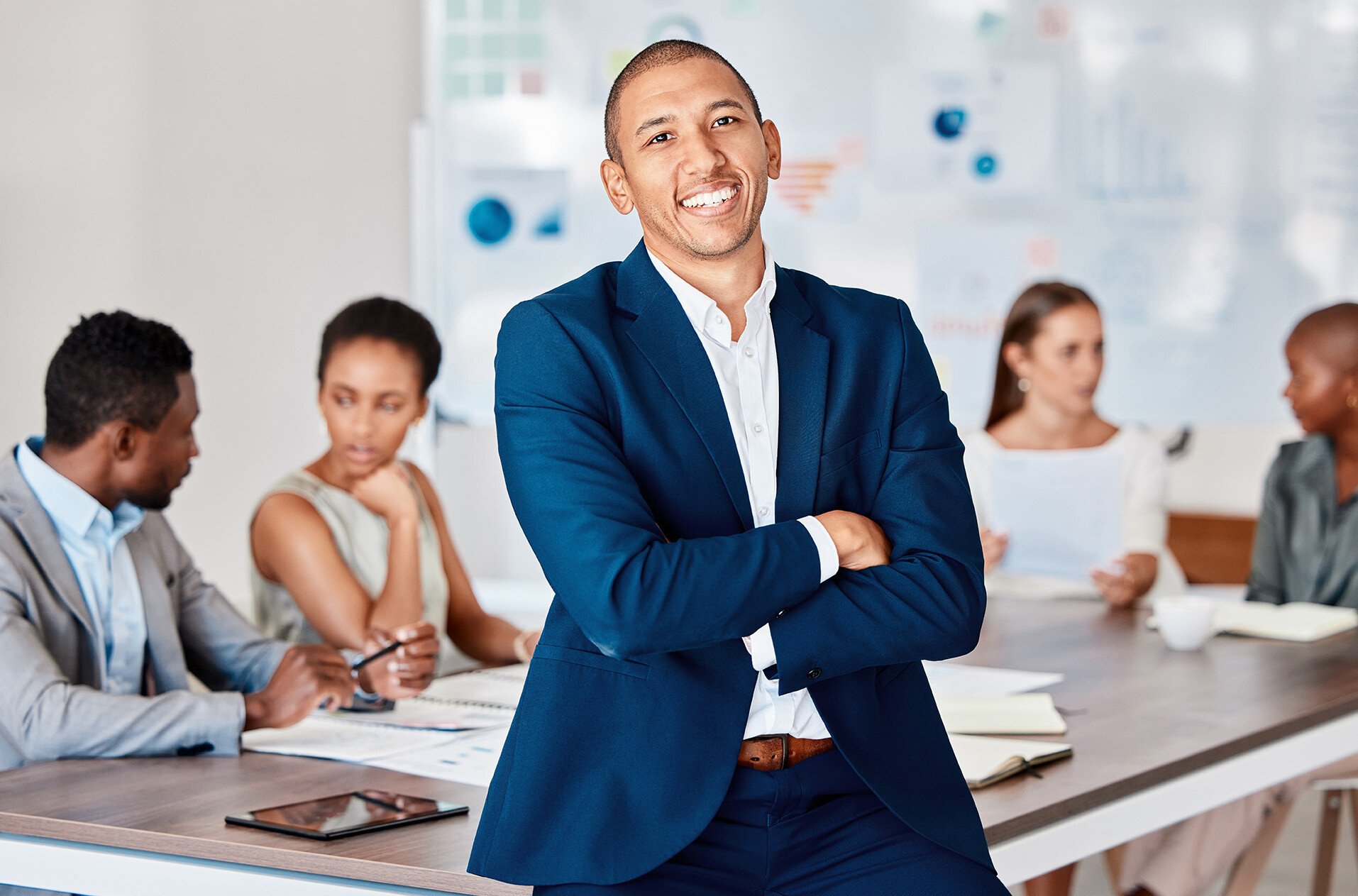 Man in suit smiling with coworkers behind him working