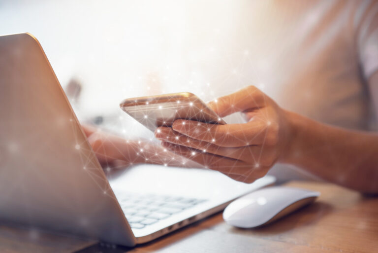 Hand holding a smartphone while using a laptop.